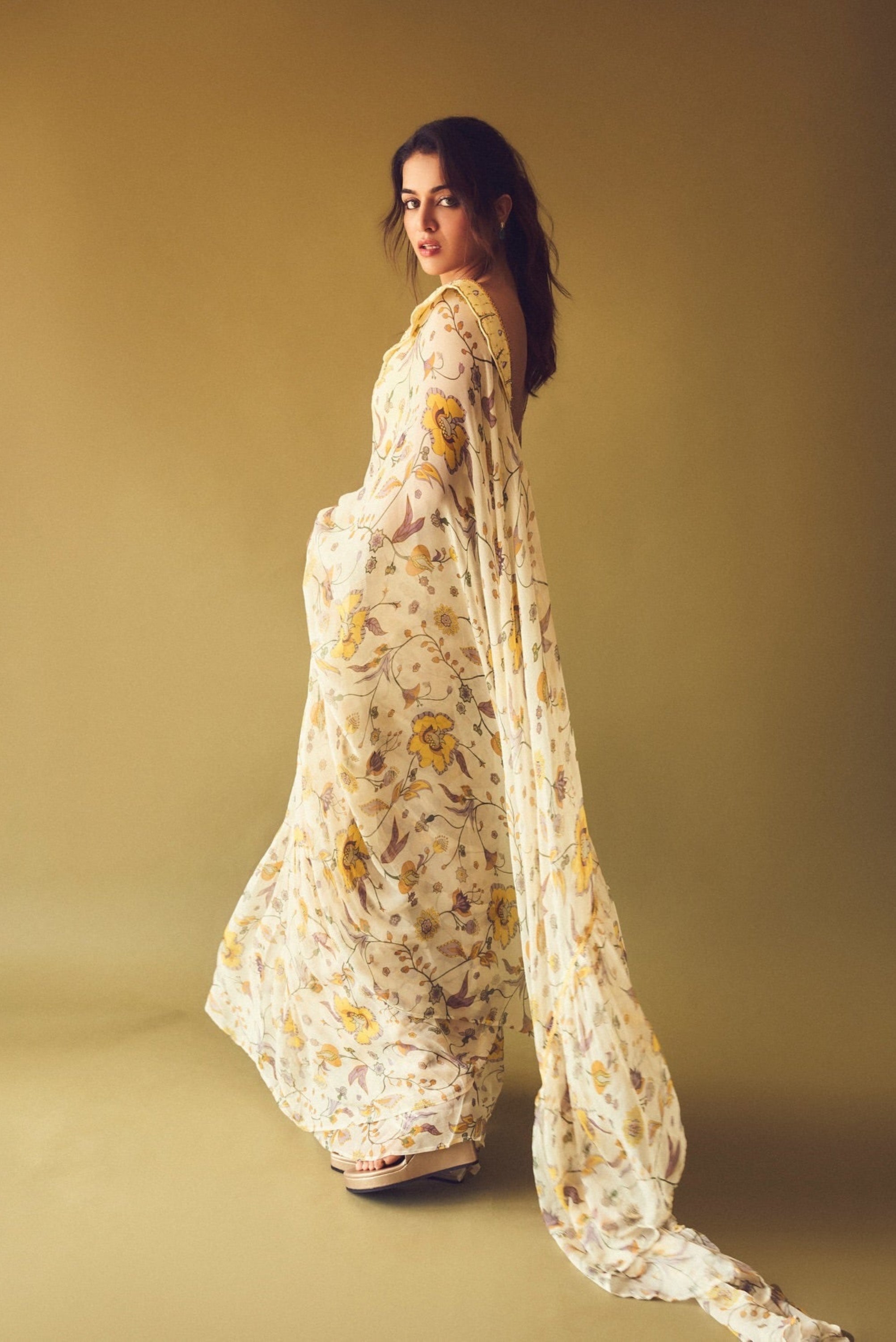 Woman in a floral saree standing against a beige background